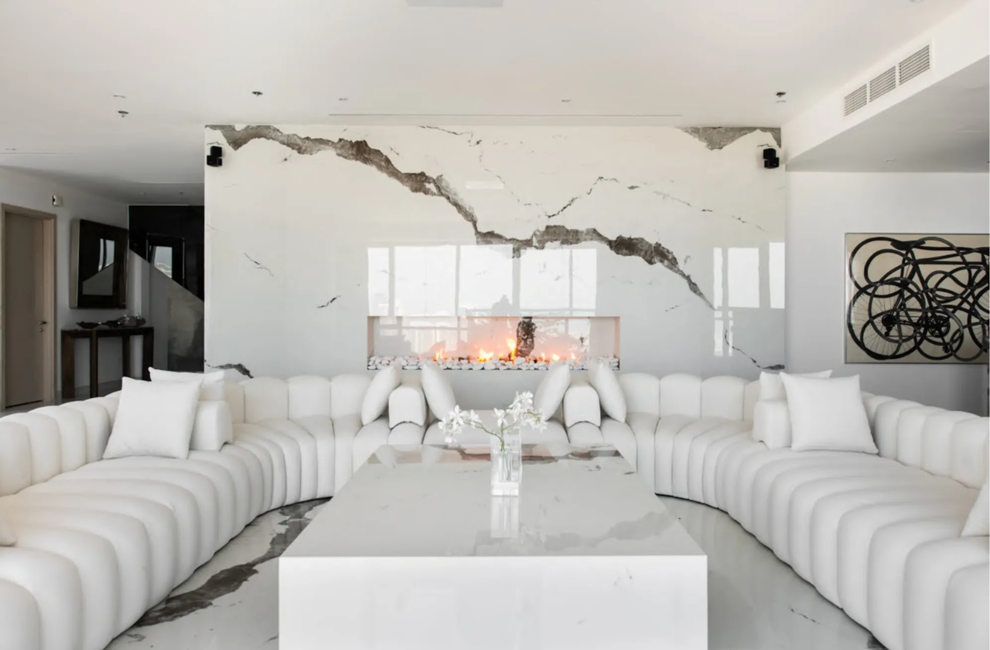 Casa Lumina living room, a curved white channel-tufted sofa facing a book-matched marble fireplace wall