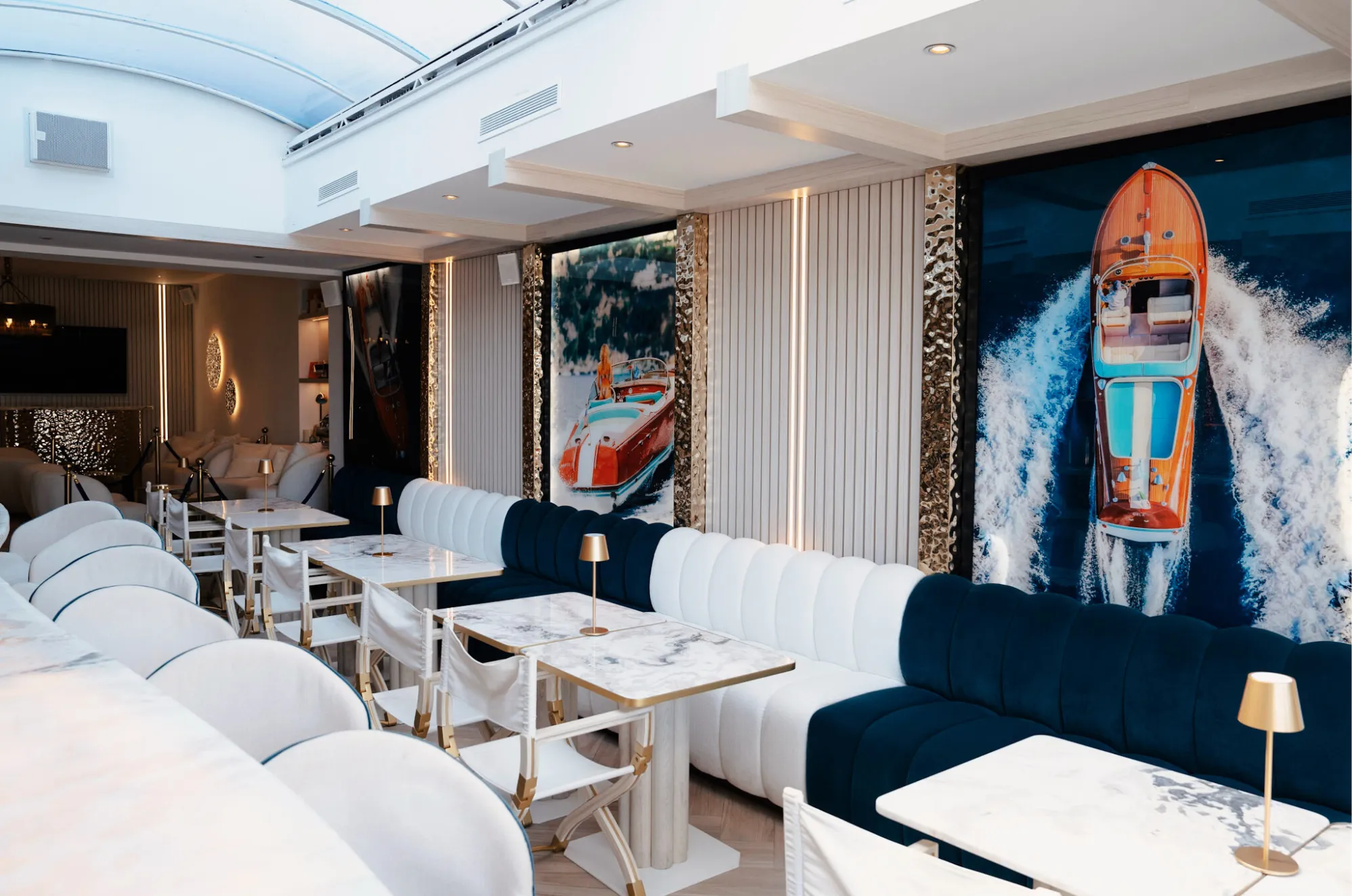 Marina Pavilion dining room with a navy and white velvet banquette, marble tables and a large speedboat print